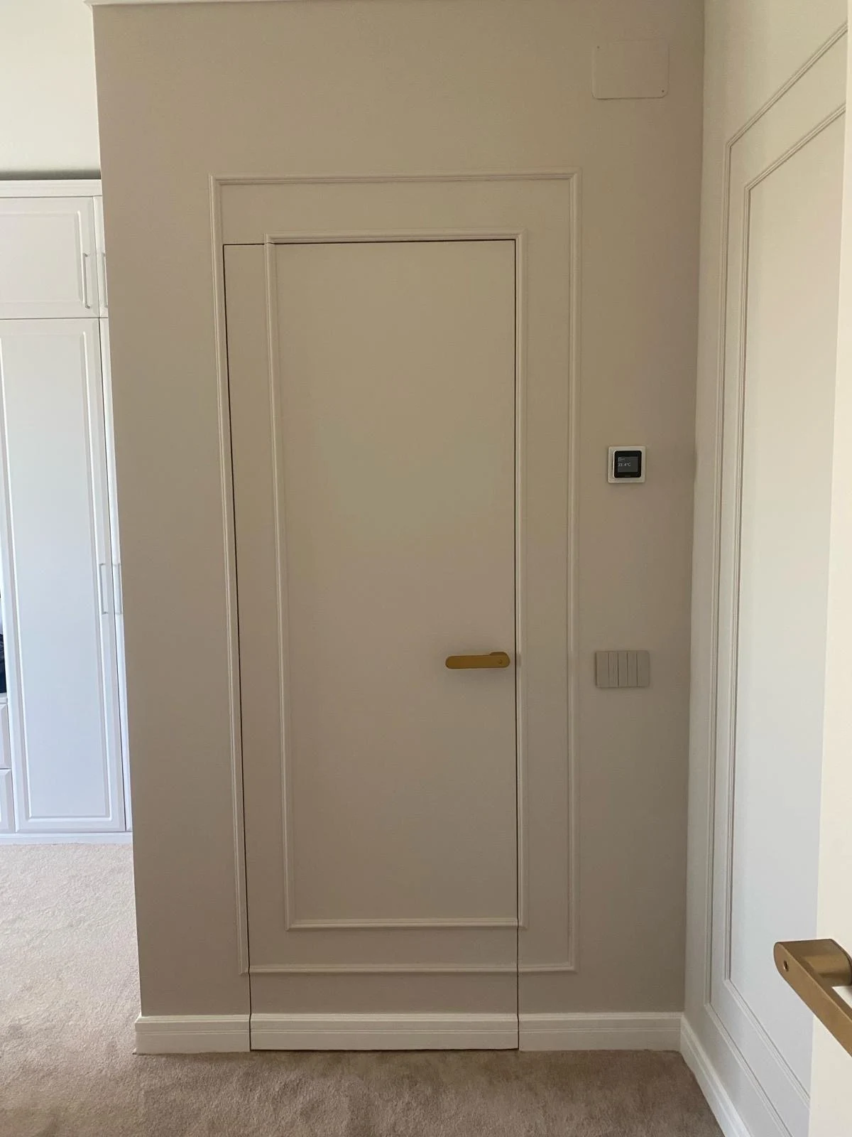 Mâner din alamă periată pe o ușă filomuro crem, încadrată de profile decorative pe perete